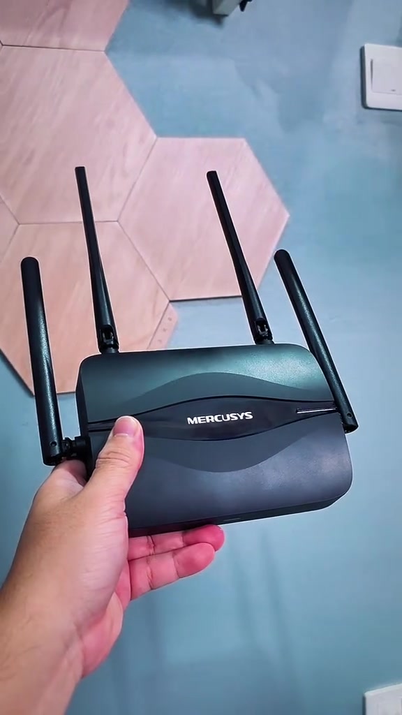 Router Mercusys MR25BE berwarna hitam dengan empat antena dipegang pada satu tangan