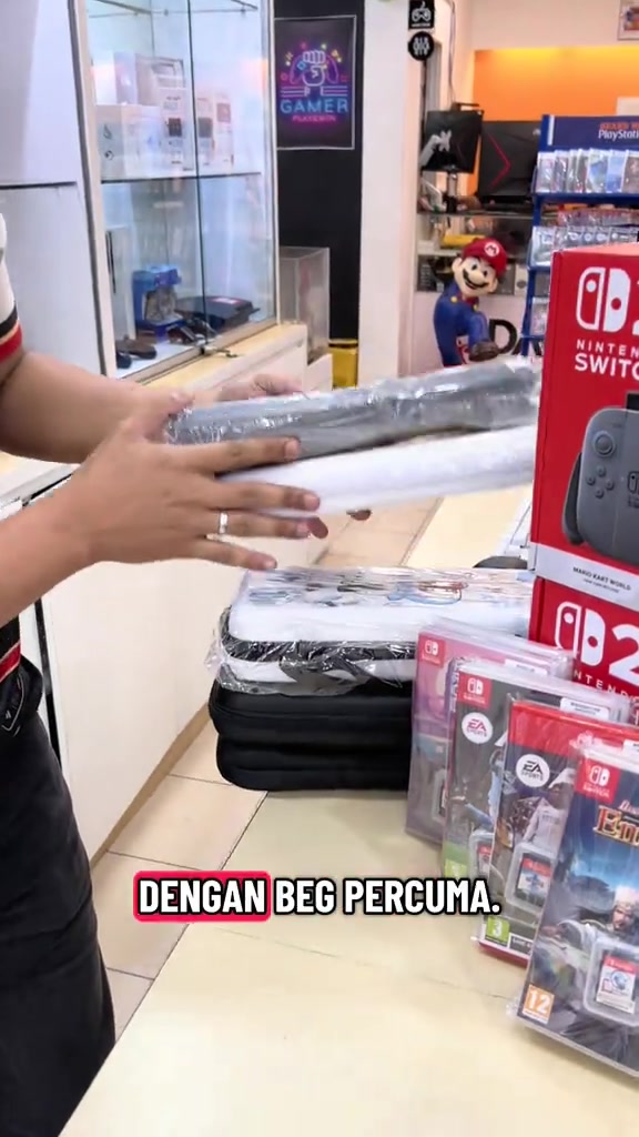 Staf kedai menunjukkan beg pouch percuma yang disertakan dengan combo Switch 2 secondhand, bersebelahan kotak Switch 2 dan game card