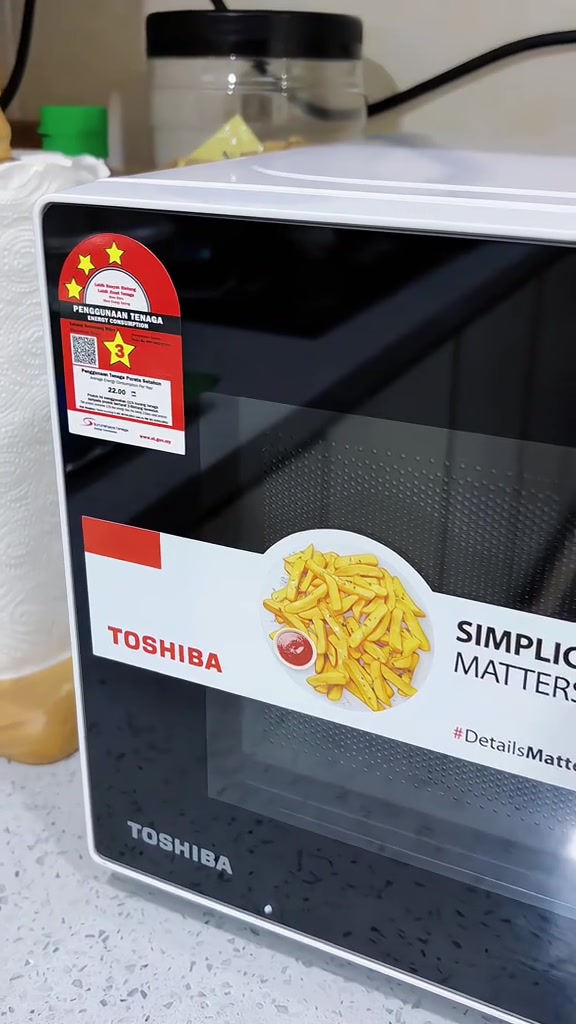 Microwave putih Toshiba di atas counter dengan label bintang penjimatan tenaga di penjuru pintu kaca