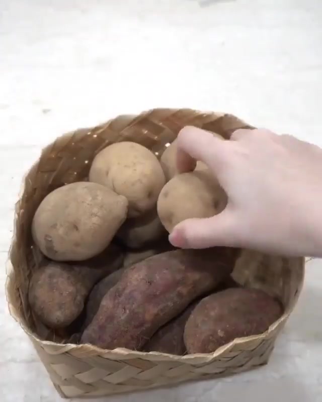 Tangan mengambil biji kentang dari bakul anyaman rotan yang penuh dengan kentang dan ubi keledek