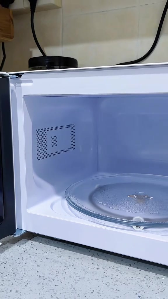 Rongga dalam microwave putih dengan turntable kaca, pintu terbuka di atas counter batu
