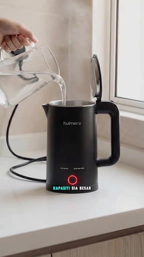 Tangan menuang air dari jag kaca ke dalam cerek elektrik hitam dengan lampu gelang merah menyala