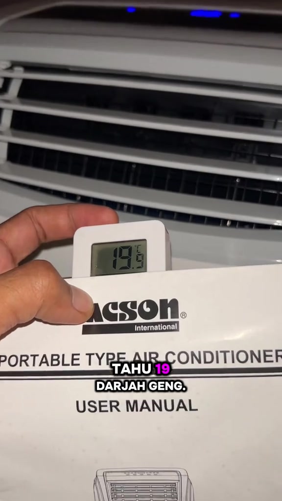 Tangan memegang termometer digital bacaan 19.9 darjah Celsius di depan grill portable aircond Acson bersama buku manual
