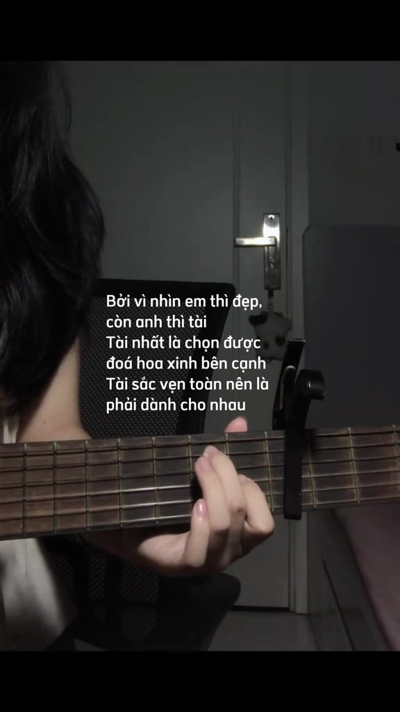 Cận cảnh bàn tay bấm hợp âm trên cần đàn guitar acoustic có kẹp capo, kèm dòng lyric Trong Đôi Mắt Thiếu Nữ trong clip cover quay trong phòng
