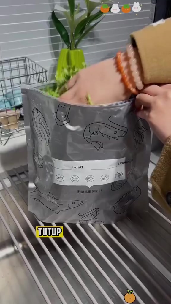 Tangan menutup zip beg aluminium foil berwarna perak yang berisi sayur hijau di atas rak dapur