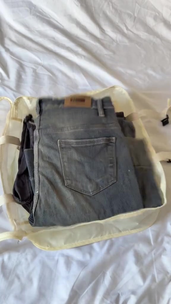 Seluar jeans dilipat kemas di dalam packing cube berpanel mesh yang diletak atas cadar putih