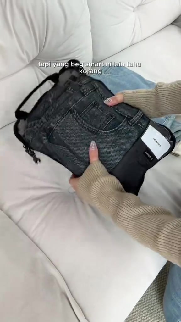 Sepasang tangan memegang packing cube compression berwarna hitam dengan seluar jeans kelihatan melalui panel mesh selepas dimampat