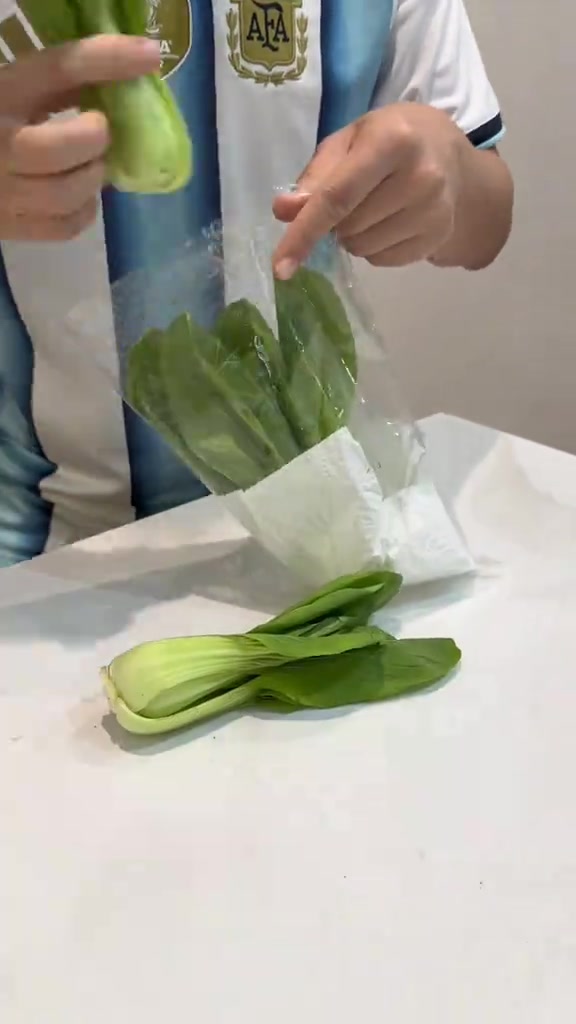 Dua tangan memasukkan sayur pak choi ke dalam beg plastik jernih yang sudah dialas tisu dapur putih di bahagian bawah