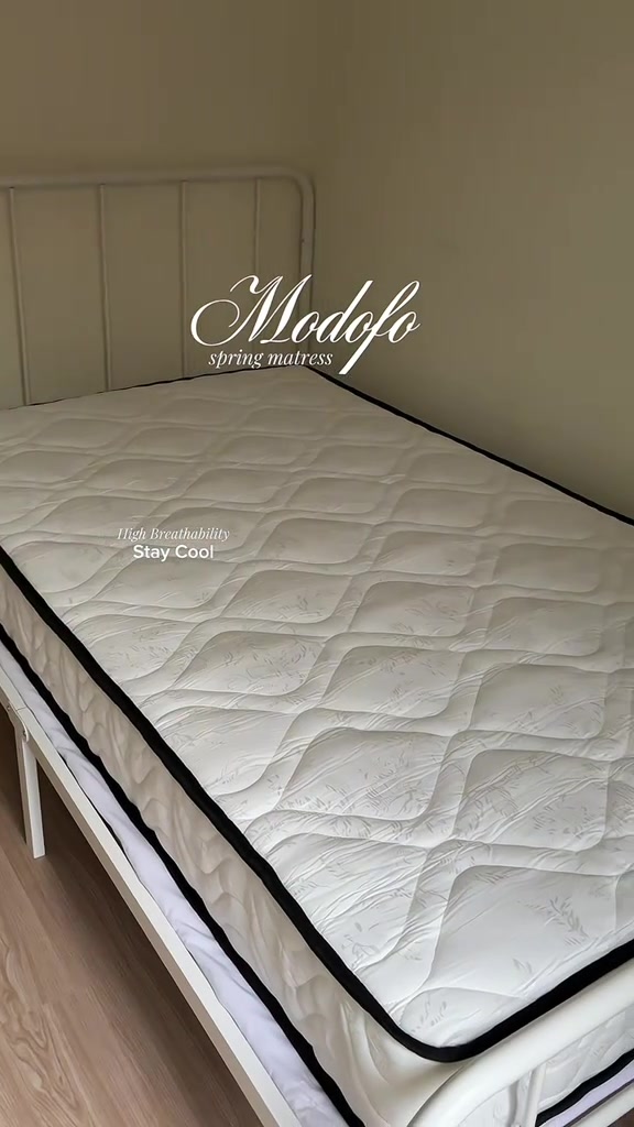 Permukaan tilam quilted putih bertepi hitam atas rangka katil besi putih, pandangan dekat dari hujung katil
