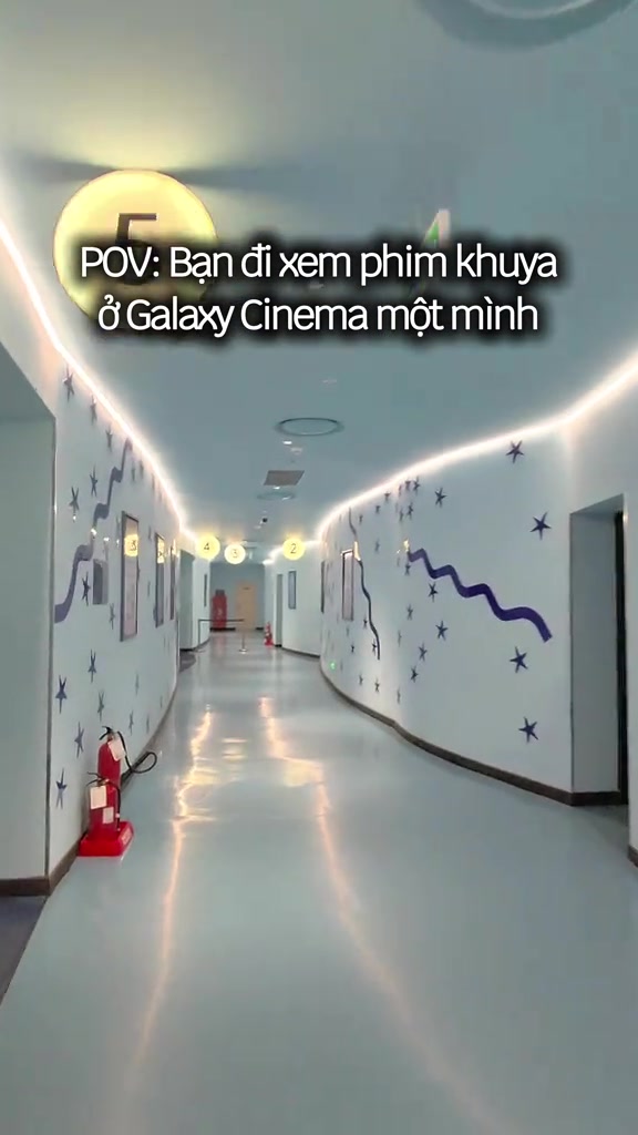 Hành lang dẫn vào các phòng chiếu của một rạp Galaxy, tường trắng trang trí ngôi sao tím và đèn số phòng vàng, không có người