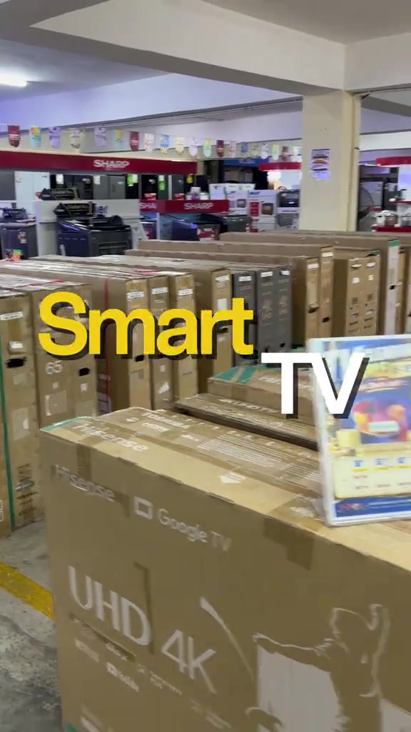 Susunan kotak TV Hisense berlabel Google TV dan UHD 4K di dalam stor kedai elektrik dengan kotak-kotak TV lain bertindan di latar belakang