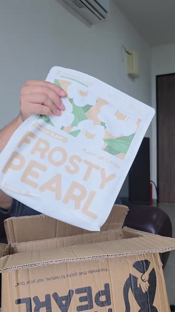 Sebelah tangan mengangkat satu pek pasir kucing Frosty Pearl dari kotak penghantaran yang terbuka