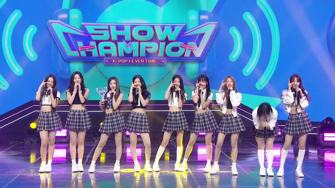 Chín thành viên A2O LITE xếp hàng ngang chào kết màn trên sân khấu Show Champion ngày 21/10, một thành viên cúi gập người cảm ơn, cúp chiến thắng nằm ở giữa hàng