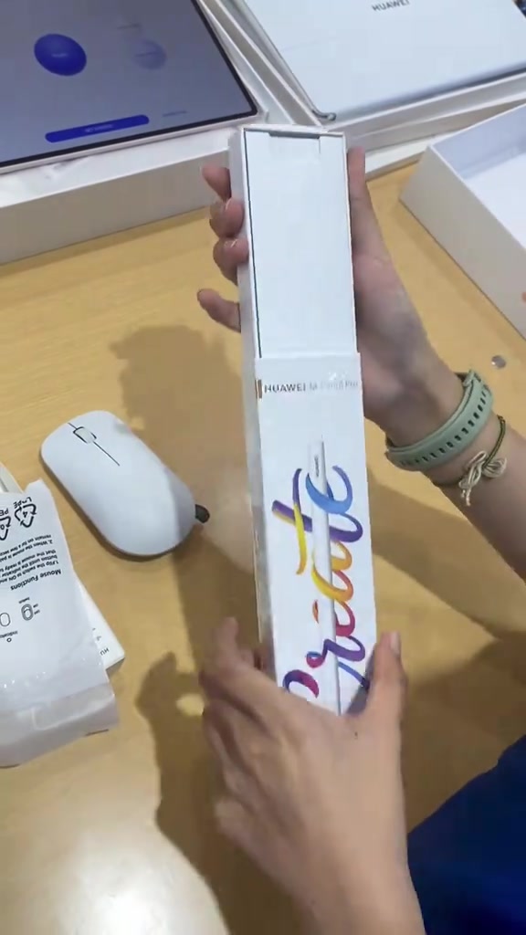 Tangan membuka kotak HUAWEI M-Pencil Pro dengan wireless mouse putih dan kotak aksesori lain di atas meja kedai