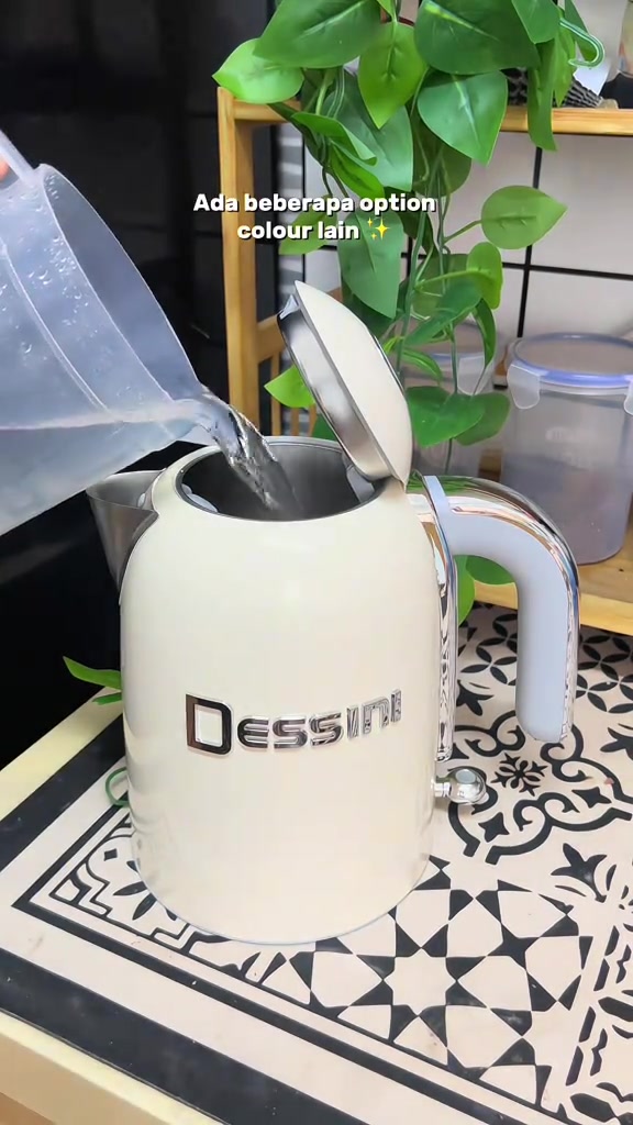 Tangan menuang air dari jag plastik ke dalam cerek elektrik Dessini warna krim dengan penutup terbuka
