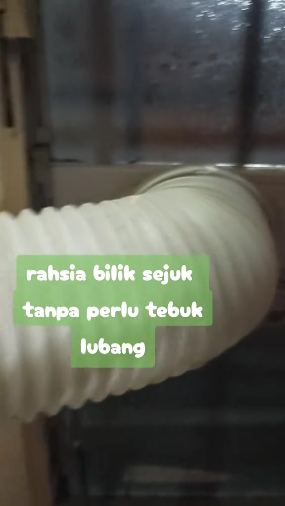 Hose putih berlingkar portable aircond disalurkan keluar melalui bukaan tingkap bergrill
