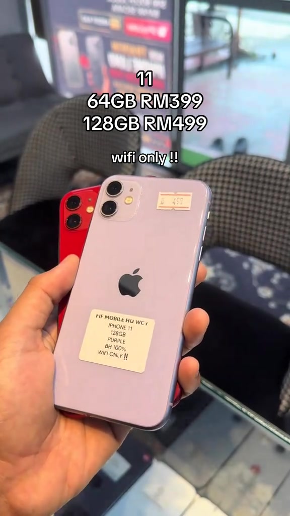 Dua iPhone 11 merah dan ungu dipegang di tangan dengan pelekat kedai bertulis BH 100% dan WIFI ONLY, serta teks harga 64GB RM399 dan 128GB RM499