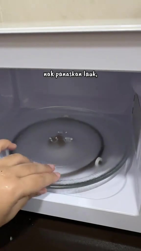 Tangan meletakkan turntable kaca ke dalam rongga microwave putih