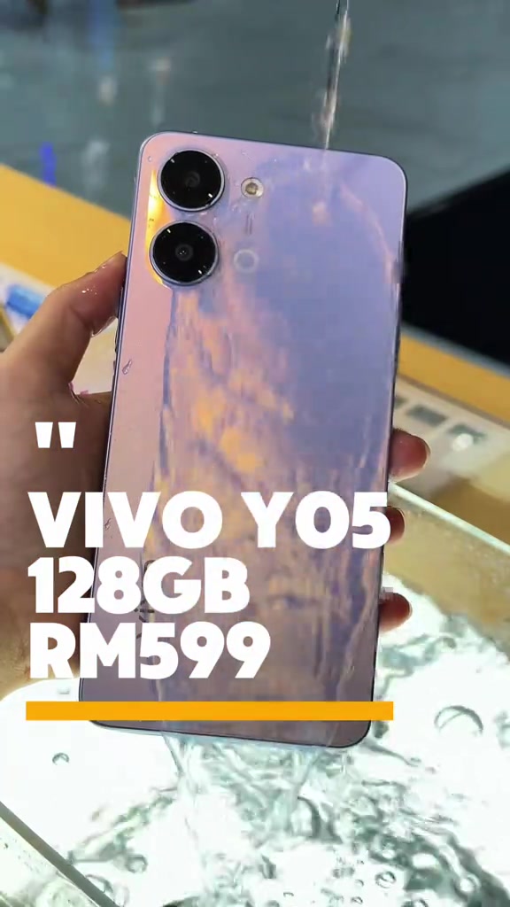 Sebuah vivo Y05 warna ungu muda dipegang di bawah aliran air sebagai demo kalis air, dengan teks VIVO Y05 128GB RM599