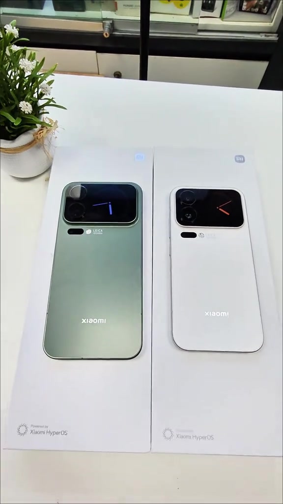 Xiaomi 17 Pro Max màu xanh và Xiaomi 17 Pro màu trắng đặt trên hai hộp trắng, màn hình phụ phía sau cả hai hiện đồng hồ
