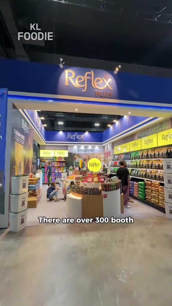 Booth jenama makanan kucing di ekspo dengan rak penuh beg kibbles berwarna-warni