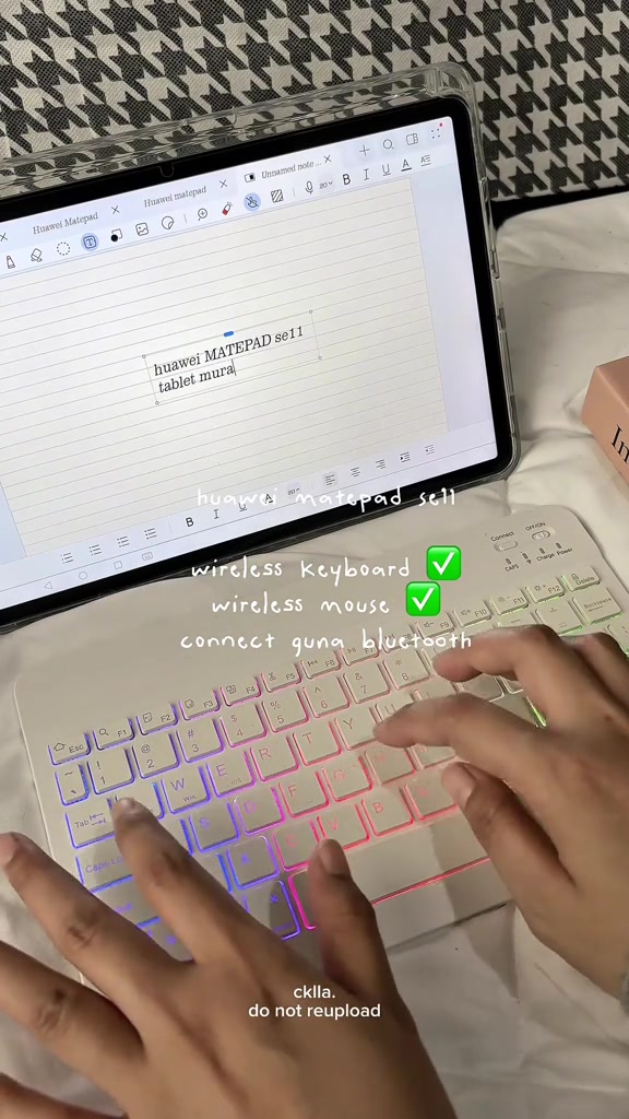 Tablet dalam case jernih disambung keyboard wireless berlampu RGB, dua tangan sedang menaip nota