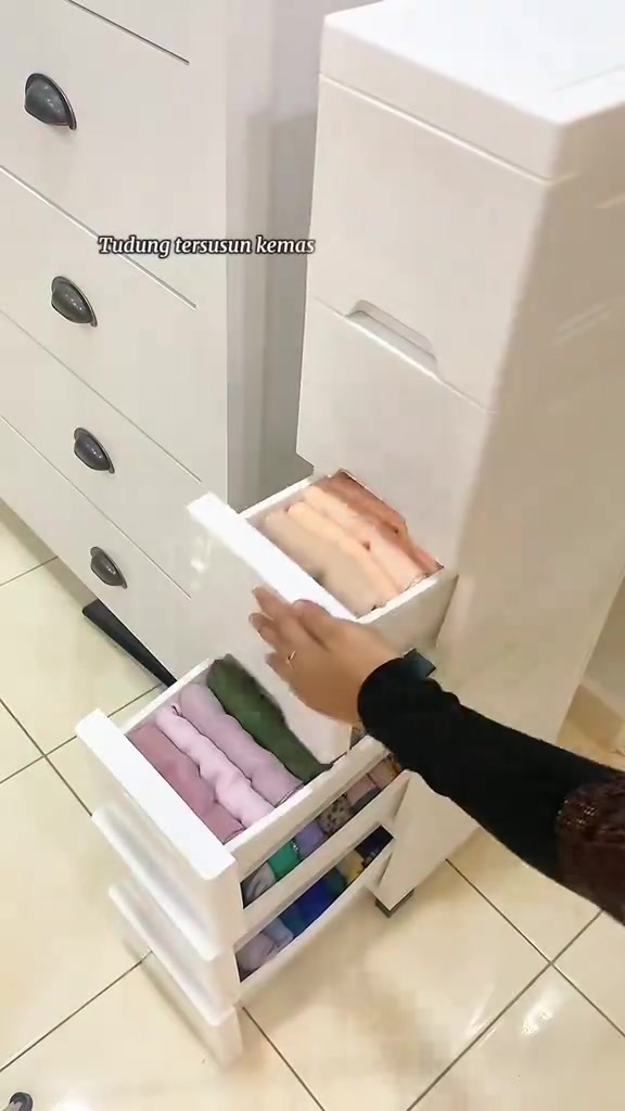 Tangan menarik laci drawer tudung putih yang tersusun kemas di sebelah almari