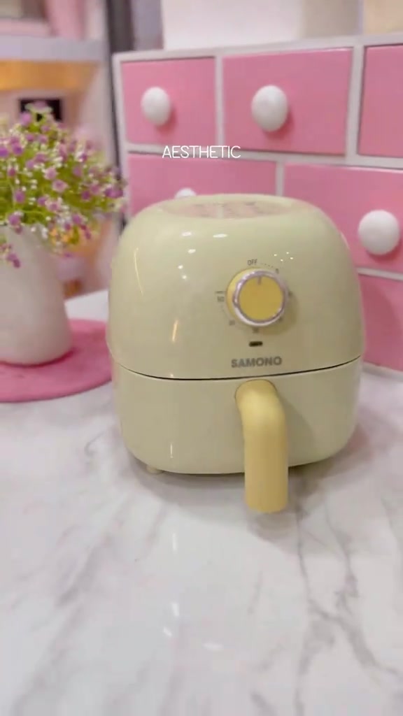 Air fryer mini kuning muda bertombol tunggal atas meja marble hadapan laci merah jambu
