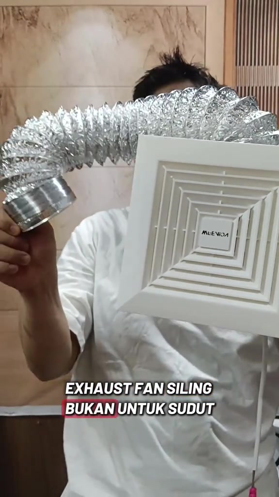 Seorang lelaki memegang unit exhaust fan siling putih dengan duct fleksibel aluminium bersambung di belakangnya