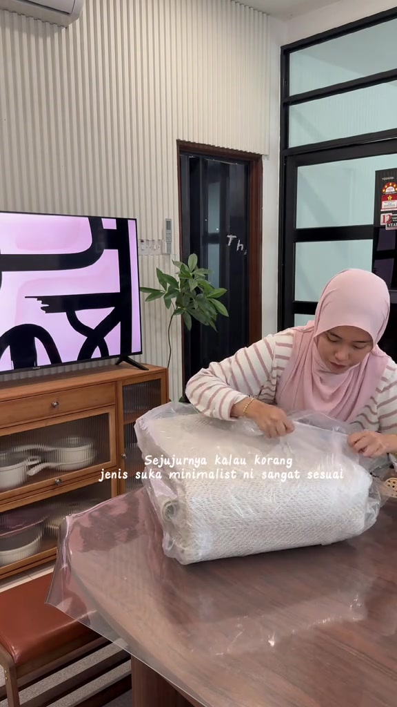 Karpet fabrik baru masih bergulung dalam bungkusan plastik diletak atas meja makan kayu