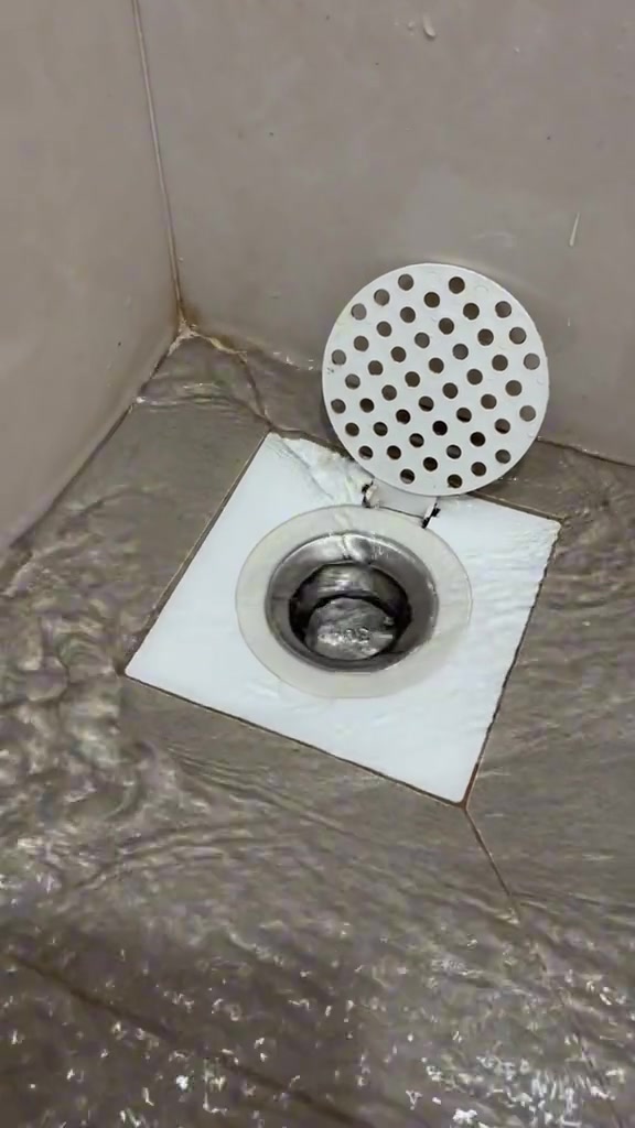 Air mengalir masuk ke lubang floor trap tandas yang terbuka dengan penutup bulat berlubang berengsel terangkat ke atas