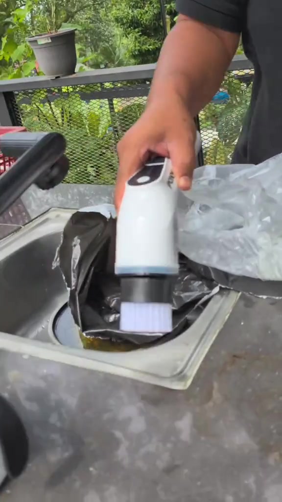 Tangan memegang pemegang berus elektrik dengan kepala berus kecil putih di atas sinki stainless steel