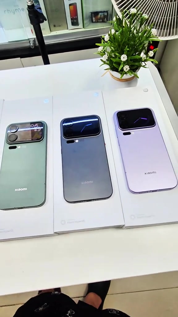 Ba chiếc Xiaomi 17 Pro Max màu xanh, xám và tím đặt trên hộp trắng trên quầy cửa hàng, mặt lưng hướng lên lộ màn hình phụ