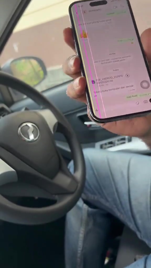 Tangan memegang telefon di dalam kereta menunjukkan chat WhatsApp dengan fail ZIP bernama PDF_X4ERDQ_20261009125224.zip dan mesej meminta membuka komputer untuk semak