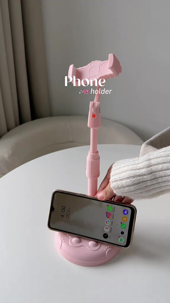 Stand meja berwarna merah jambu dengan tapak bulat memegang telefon di atas meja putih