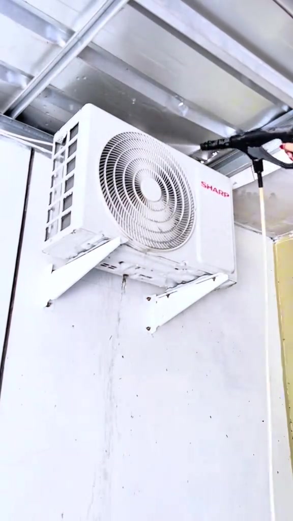 Unit outdoor aircond Sharp disembur dari luar dengan lance penyembur tekanan