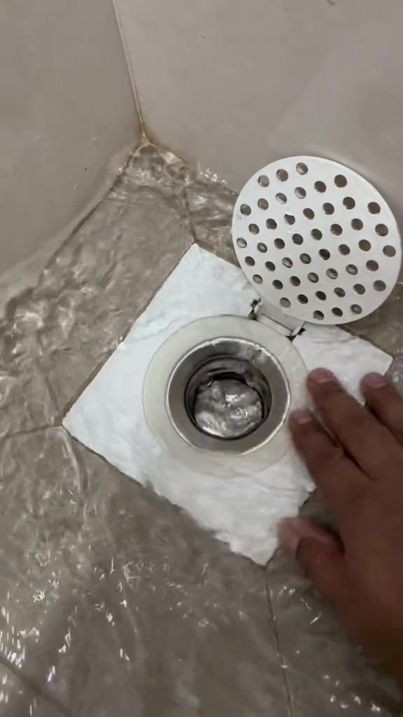 Tangan di sisi floor trap berlantai jubin basah dengan penutup bulat berlubang berengsel terbuka menampakkan core stainless di dalamnya