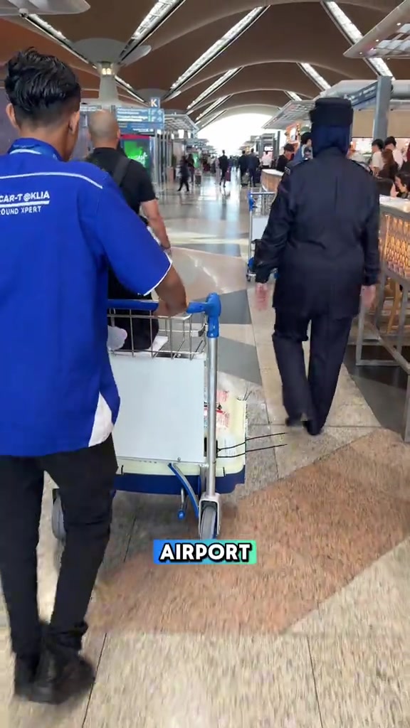 Staf lapangan terbang menolak troli membawa crate kucing melalui dewan check-in KLIA selepas urusan daftar masuk selesai