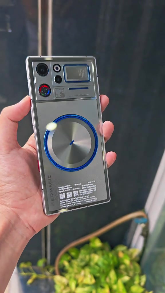 Mặt lưng bạc của RedMagic 12 Pro+ với vòng quạt viền xanh và tem thông số model, cầm trên tay trước cửa shop