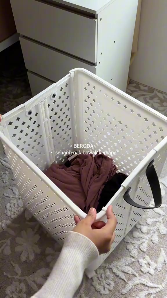 Tangan memegang tepi bakul baju plastik putih berlubang berisi baju coklat dari pandangan atas
