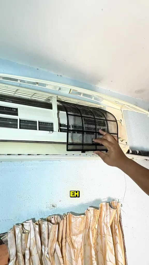 Tangan mengeluarkan filter aircond berwarna hitam yang berdebu dari unit dinding