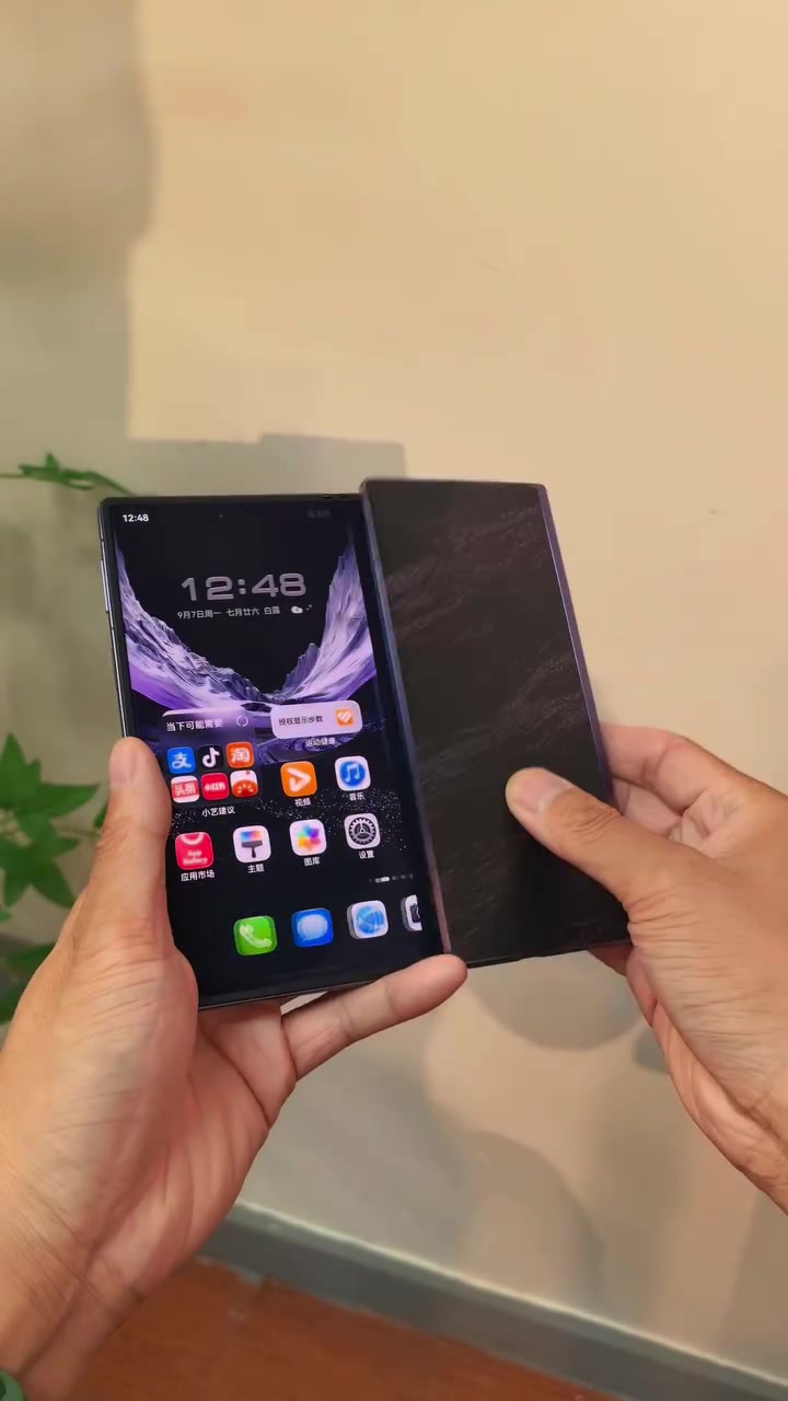 Điện thoại gập ba Huawei mở một phần, màn hình chính HarmonyOS với các biểu tượng ứng dụng tiếng Trung và kho ứng dụng AppGallery