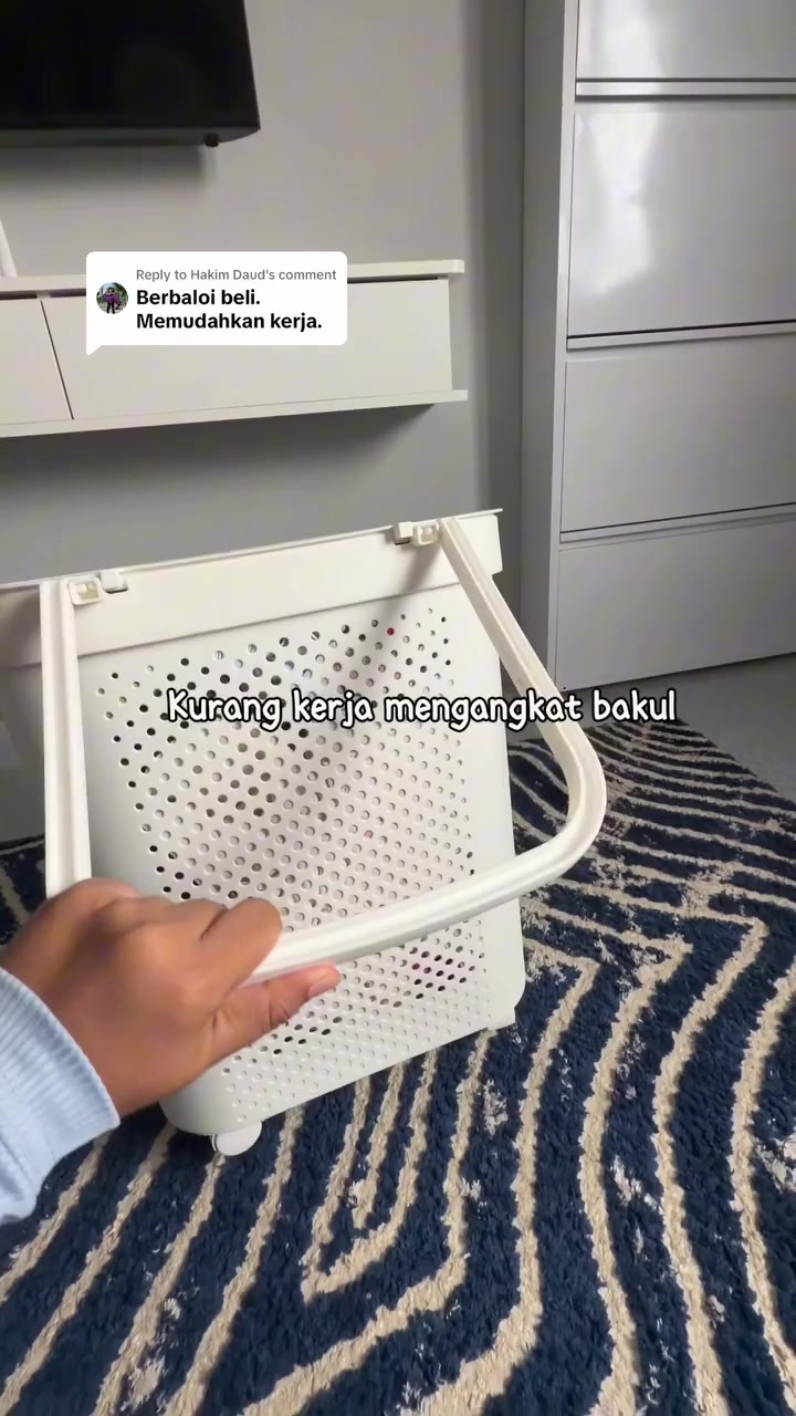 Tangan memegang tangkai tarik bakul baju putih berlubang yang dicondongkan menunjukkan roda kecil di bawah