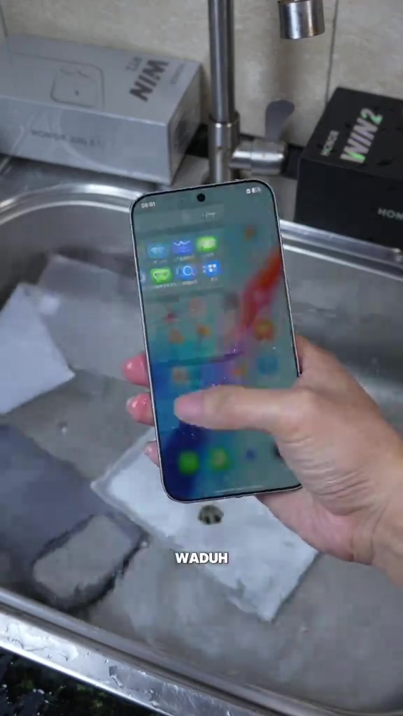 HONOR WIN 2 dipegang dengan skrin hidup di atas sinki, kotak putih dan kotak hitam WIN 2 di latar belakang
