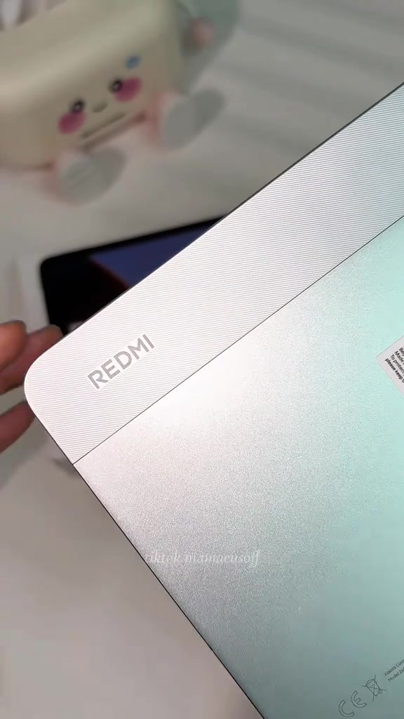 Tutup belakang Redmi Pad 2 warna mint dengan logo REDMI, dipegang dengan satu tangan