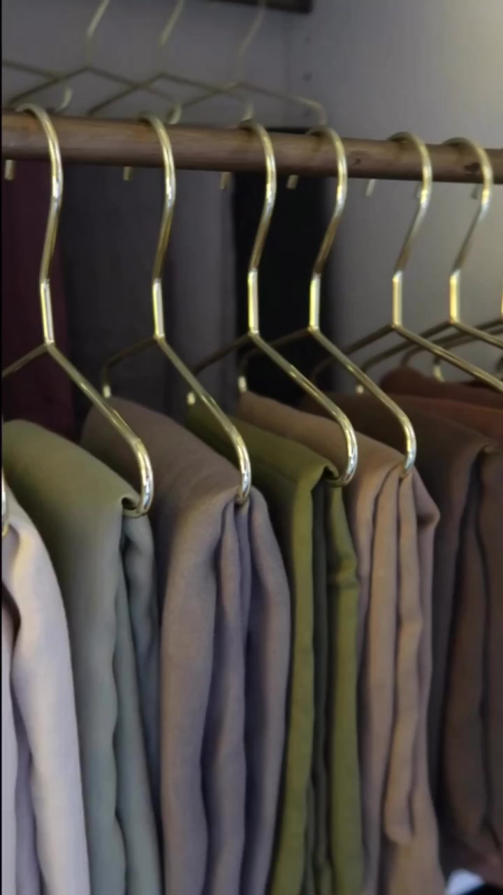 Hanger emas tergantung pada rod kayu dengan tudung fabrik warna neutra tersusun