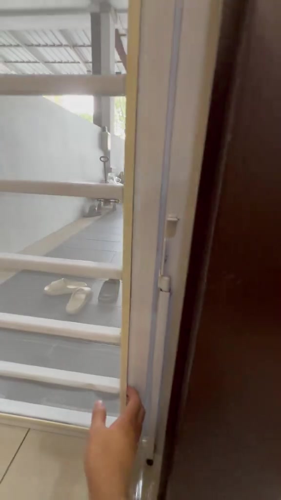 Tangan menyentuh tepi bingkai skrin jaring putih di ruang pintu dengan laluan luar berjersi kelihatan di belakang