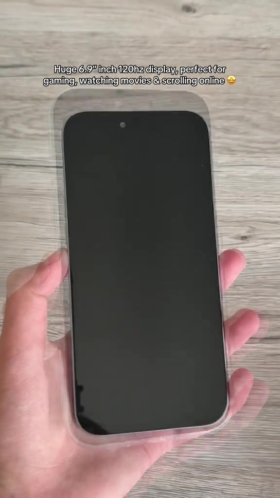 Bahagian depan OUKITEL C17 Plus dengan skrin padam dipegang sebelah tangan di atas latar kayu