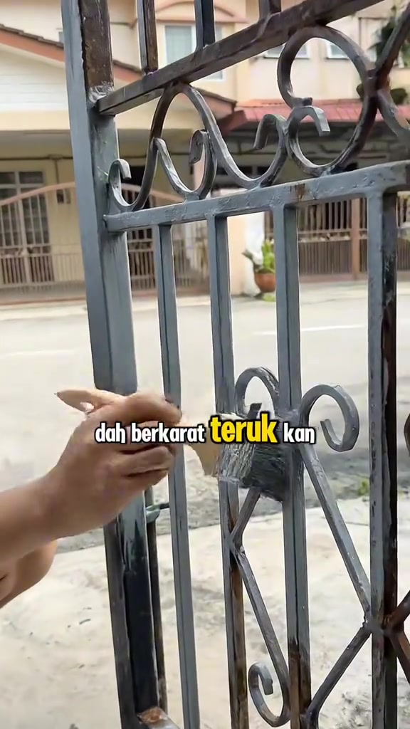 Tangan menyapu cat kelabu dengan berus ke atas pagar besi berhias yang dah berkarat teruk