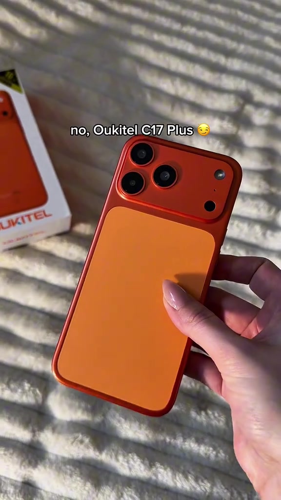 OUKITEL C17 Plus warna oren dilihat dari belakang dipegang sebelah tangan, kotak pembungkusan di sebelah kiri